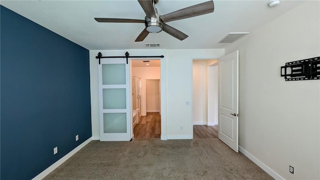 unfurnished bedroom featuring ceiling fan, a barn door, and carpet floors