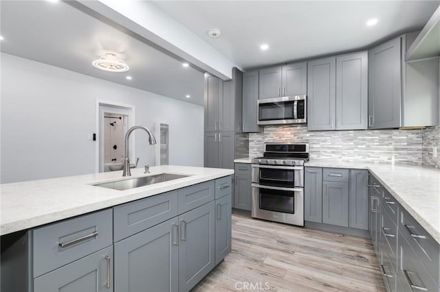 kitchen with a sink, tasteful backsplash, light wood-type flooring, gray cabinetry, and appliances with stainless steel finishes