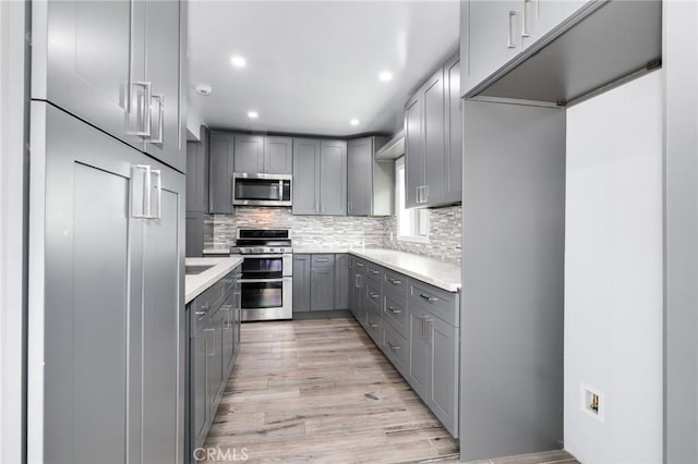 kitchen featuring stainless steel appliances, light countertops, decorative backsplash, gray cabinetry, and light wood-style flooring