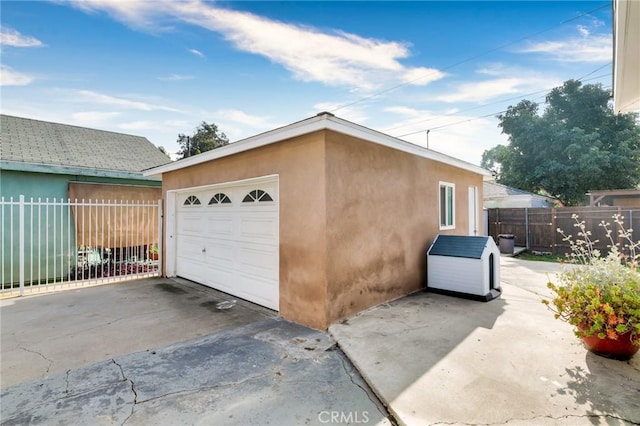 detached garage featuring concrete driveway and fence
