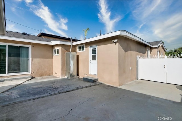 rear view of house featuring a gate, a patio area, stucco siding, and fence