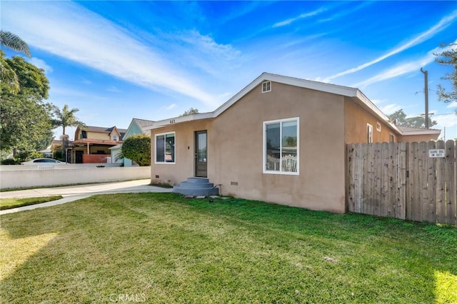 back of property with stucco siding, fence, and a lawn