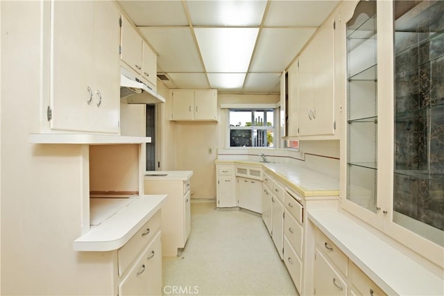 kitchen featuring light floors, light countertops, cream cabinets, a sink, and under cabinet range hood