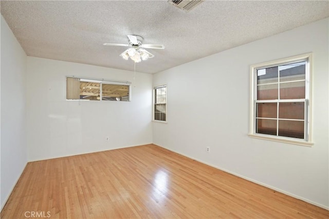 empty room featuring a ceiling fan, light wood-type flooring, visible vents, and a textured ceiling