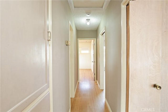 hallway with light wood-style floors, baseboards, and a textured ceiling