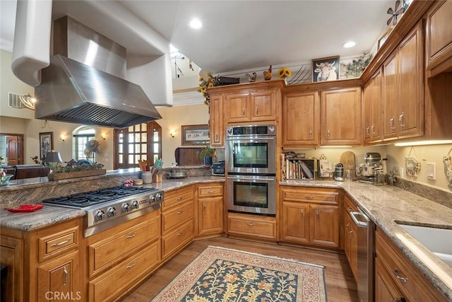 41700 Jojoba Hills Cir, Aguanga, CA 92536 - kitchen with appliances with stainless steel finishes, light hardwood / wood-style floors, light stone countertops, kitchen peninsula, and exhaust hood
