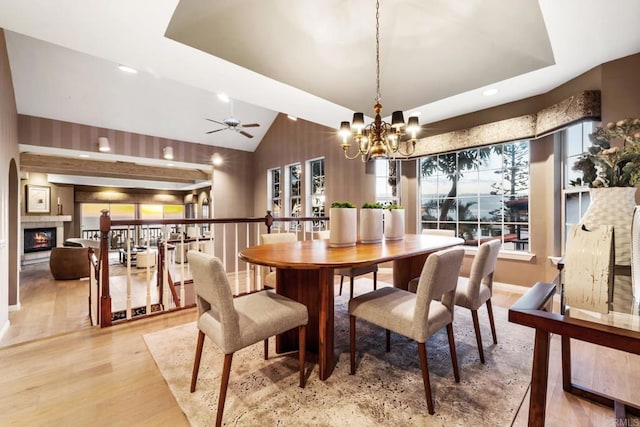 dining area featuring vaulted ceiling, ceiling fan with notable chandelier, a raised ceiling, and light hardwood / wood-style floors