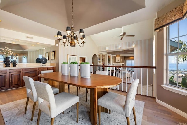 dining space with ceiling fan with notable chandelier, vaulted ceiling, and light hardwood / wood-style floors