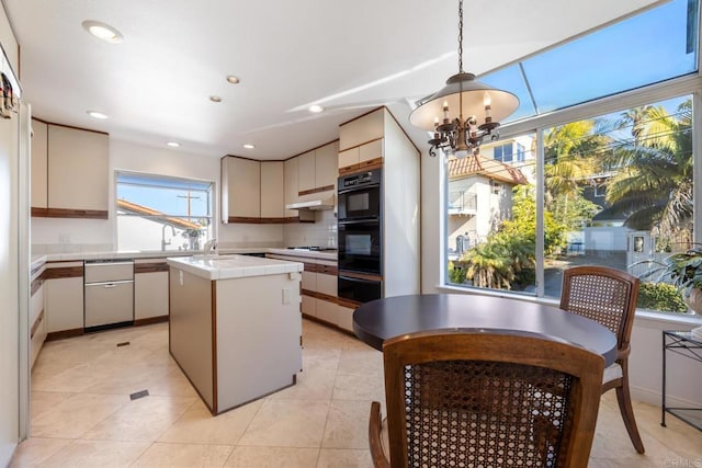 kitchen featuring an inviting chandelier, decorative light fixtures, a center island, tile counters, and decorative backsplash