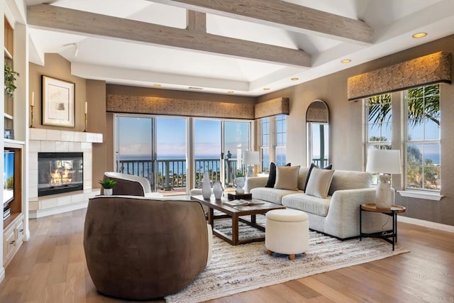 living area featuring beam ceiling, recessed lighting, wood finished floors, a tile fireplace, and baseboards