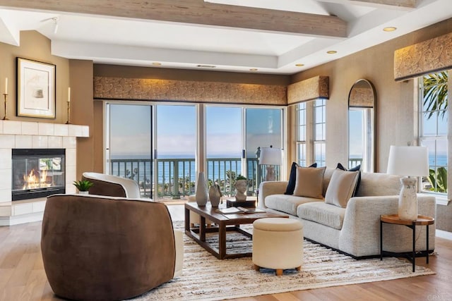 living area with a water view, wood finished floors, beamed ceiling, and a tile fireplace