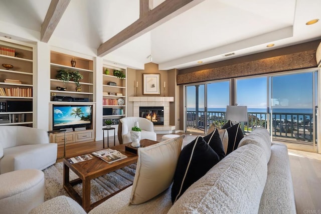 living area with visible vents, beamed ceiling, wood finished floors, a water view, and a fireplace