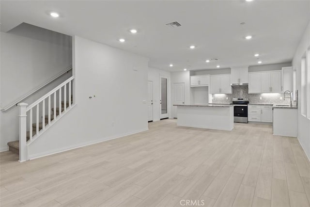 kitchen with stainless steel electric range oven, visible vents, decorative backsplash, light wood-style floors, and open floor plan