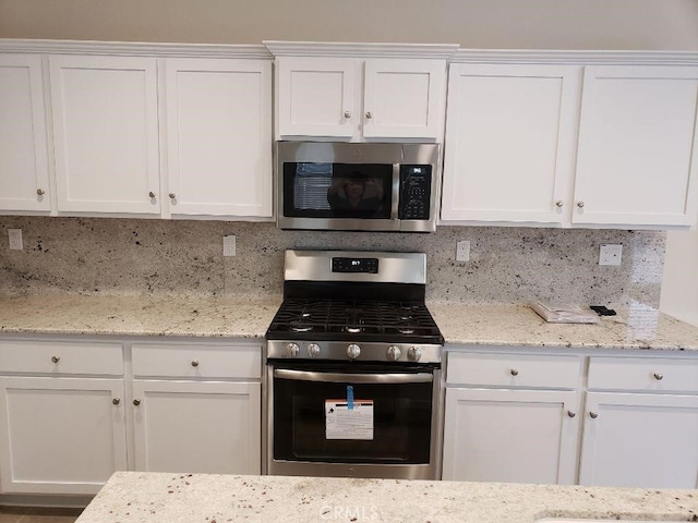 kitchen with white cabinetry, backsplash, light stone counters, and appliances with stainless steel finishes