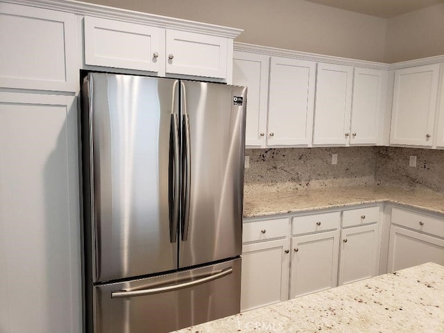 kitchen with stainless steel refrigerator, decorative backsplash, light stone counters, and white cabinets