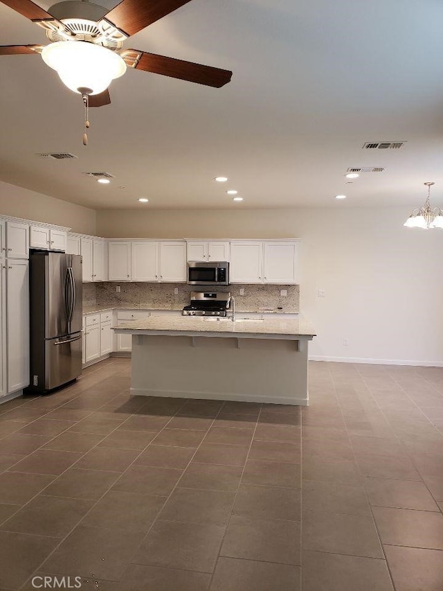 kitchen with ceiling fan, a kitchen island with sink, backsplash, stainless steel appliances, and white cabinets