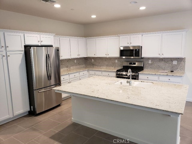 kitchen with white cabinetry, light stone countertops, stainless steel appliances, and a center island with sink