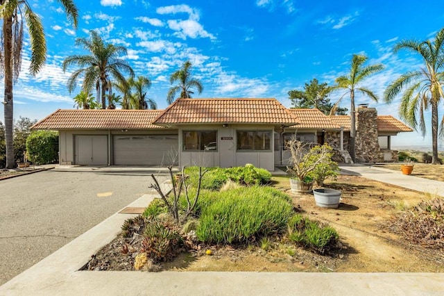 view of front of home with a garage, a chimney, driveway, and a tiled roof