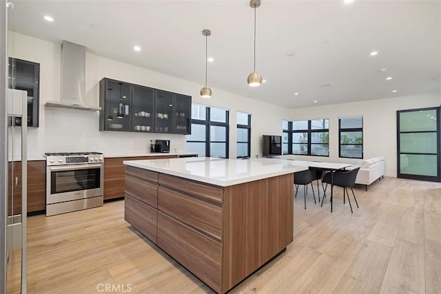 kitchen with stainless steel gas range, decorative light fixtures, a center island, light wood-type flooring, and wall chimney range hood