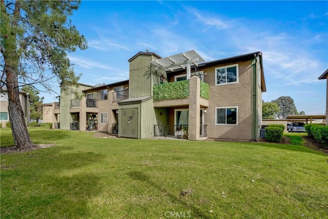 rear view of property featuring a balcony, a lawn, and stucco siding