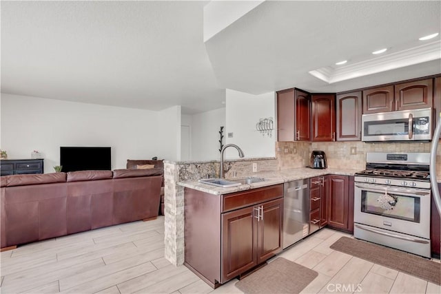 kitchen featuring a sink, backsplash, appliances with stainless steel finishes, a peninsula, and a raised ceiling