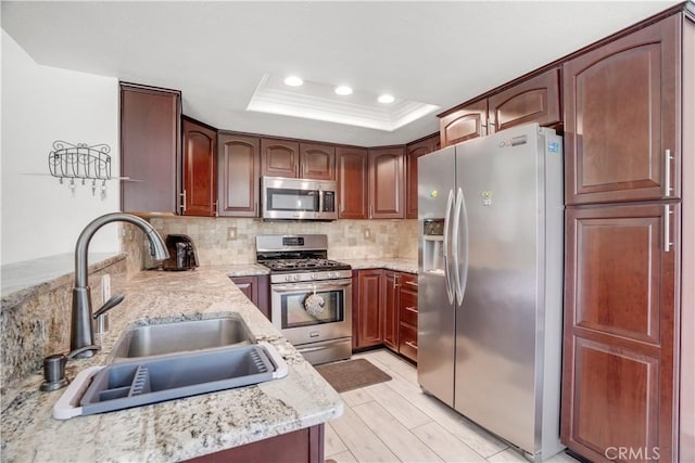 kitchen featuring light stone counters, stainless steel appliances, tasteful backsplash, a raised ceiling, and a sink