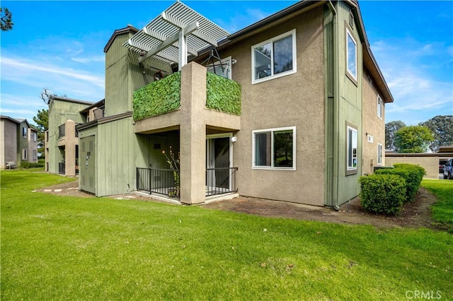 back of property featuring a balcony, a lawn, and stucco siding