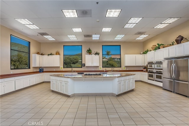 kitchen with sink, appliances with stainless steel finishes, a center island, light stone countertops, and white cabinets