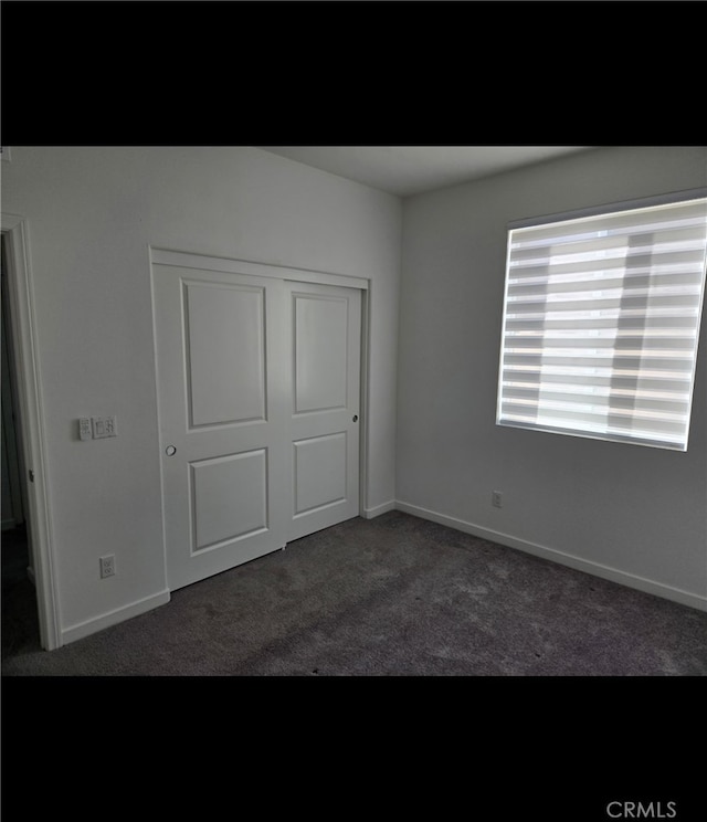 unfurnished bedroom featuring a closet and dark colored carpet