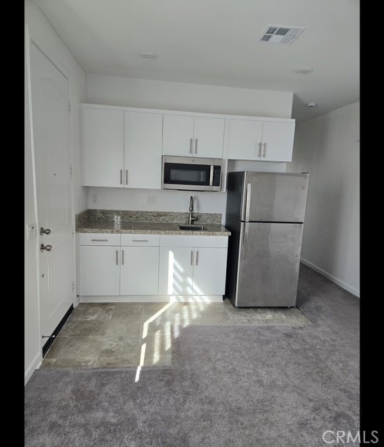 kitchen with sink, white cabinetry, light stone counters, appliances with stainless steel finishes, and light colored carpet