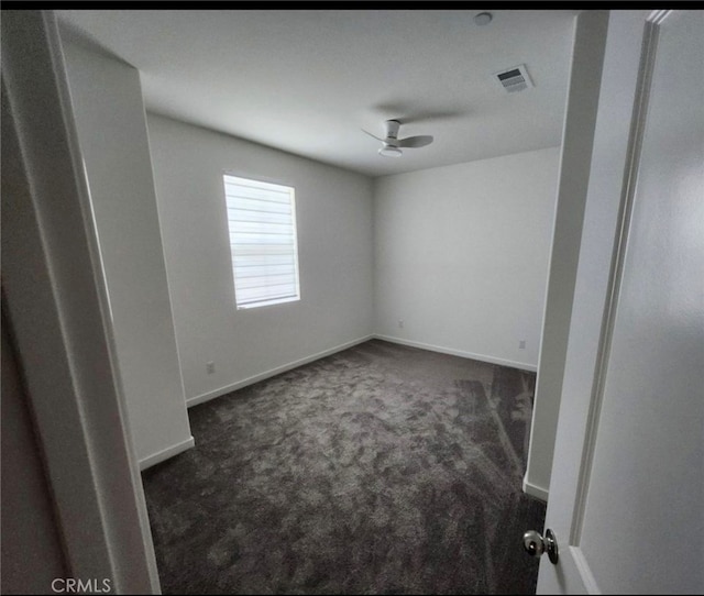 empty room featuring ceiling fan and dark colored carpet