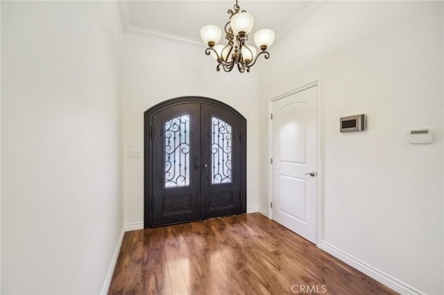 entryway with hardwood / wood-style flooring, ornamental molding, a notable chandelier, and french doors