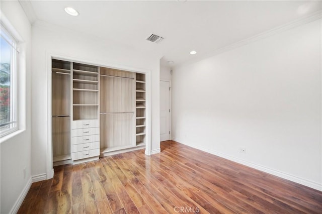 unfurnished bedroom with hardwood / wood-style flooring, crown molding, and a closet