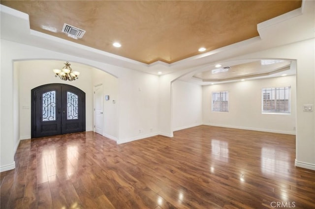 foyer featuring french doors, dark hardwood / wood-style floors, a tray ceiling, and a notable chandelier