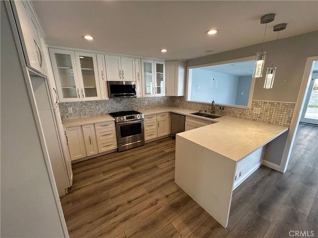 kitchen featuring dark wood-style flooring, a peninsula, appliances with stainless steel finishes, white cabinetry, and a sink