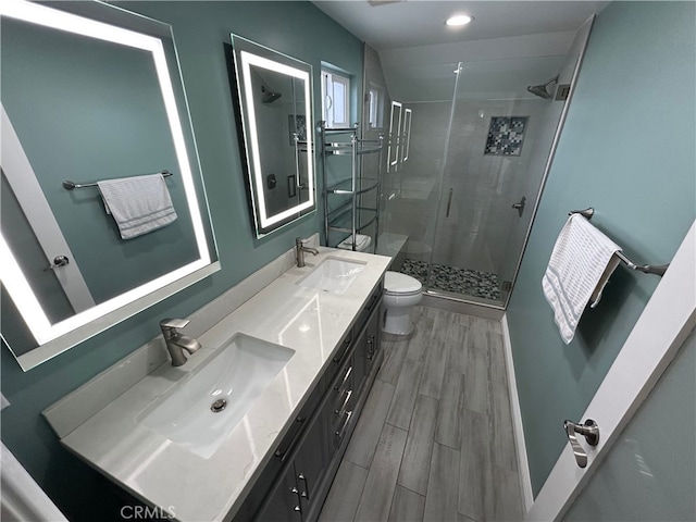 bathroom with a shower stall, double vanity, a sink, and wood finish floors