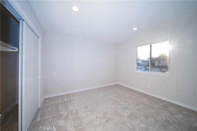 unfurnished bedroom featuring recessed lighting, a closet, light colored carpet, and baseboards