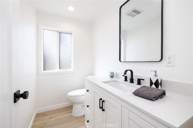 bathroom with toilet, wood finished floors, vanity, visible vents, and baseboards