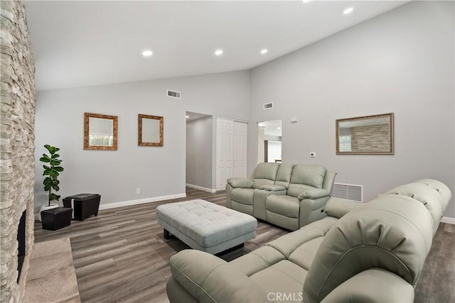 living room with hardwood / wood-style flooring, a stone fireplace, and high vaulted ceiling