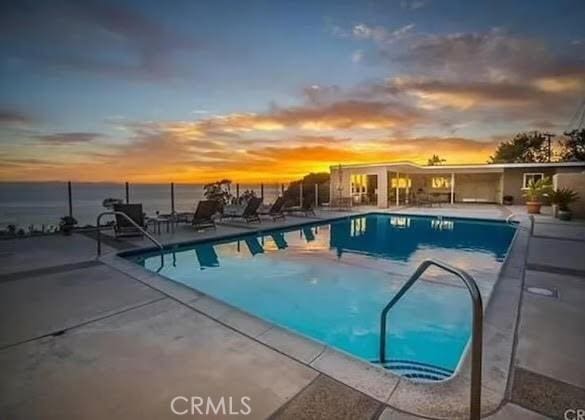 pool at dusk featuring a water view and a patio area