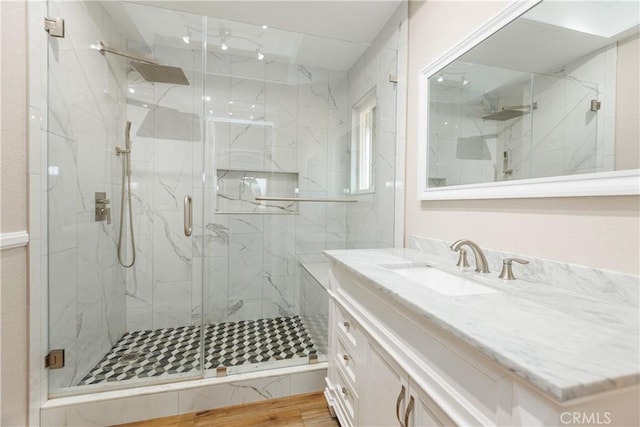 full bath with a marble finish shower, wood finished floors, and vanity