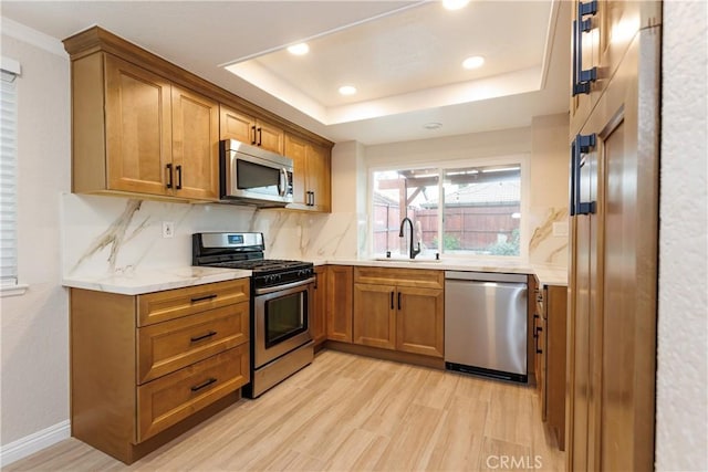 kitchen featuring a raised ceiling, stainless steel appliances, a sink, and brown cabinets