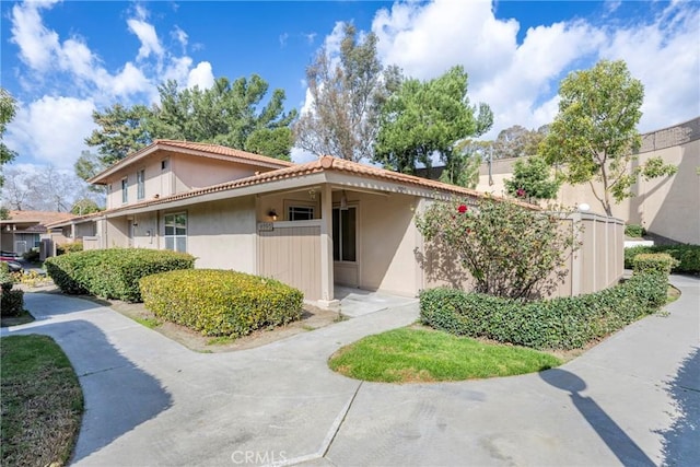 view of side of home featuring a tiled roof, fence, and stucco siding