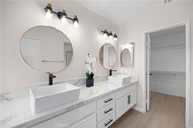 full bath with a walk in closet, wood finished floors, a sink, and double vanity