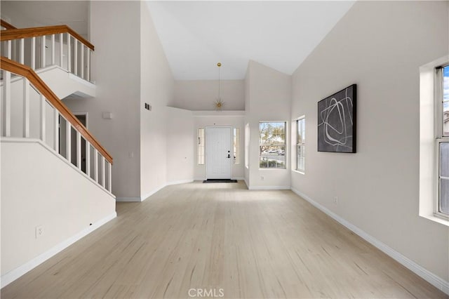 foyer entrance featuring baseboards, high vaulted ceiling, stairs, and light wood-style floors