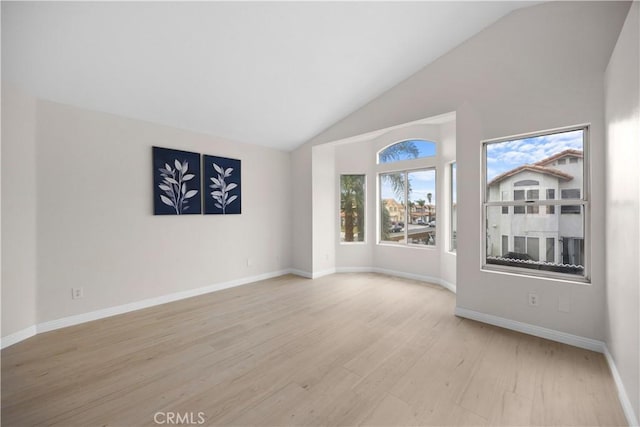 unfurnished room with high vaulted ceiling, light wood-type flooring, and baseboards