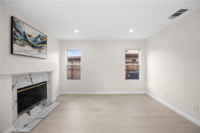 unfurnished living room with light wood-style flooring, recessed lighting, a premium fireplace, visible vents, and baseboards