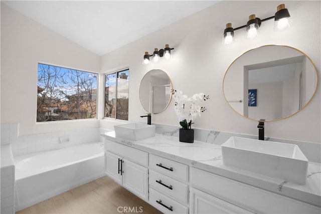 full bathroom featuring a bath, double vanity, vaulted ceiling, and a sink