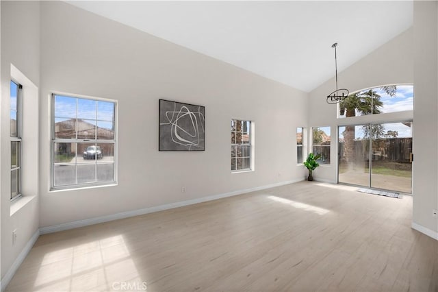 unfurnished room featuring baseboards, high vaulted ceiling, light wood-style flooring, and a notable chandelier