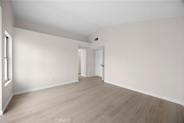 empty room with light wood-type flooring, visible vents, vaulted ceiling, and baseboards